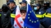 Жінка з прапорами ЄС та Грузії стоїть перед поліцією, яка блокує вулицю під час мітингу опозиції в Тбілісі, 25 листопада 2024 року