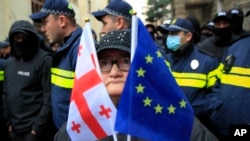 Жінка з прапорами ЄС та Грузії стоїть перед поліцією, яка блокує вулицю під час мітингу опозиції в Тбілісі, 25 листопада 2024 року