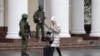 Женщина проходит мимо вооруженных людей в военной форме без опознавательных знаков, блокировавших аэропорт Симферополя. 28 февраля 2014 года.